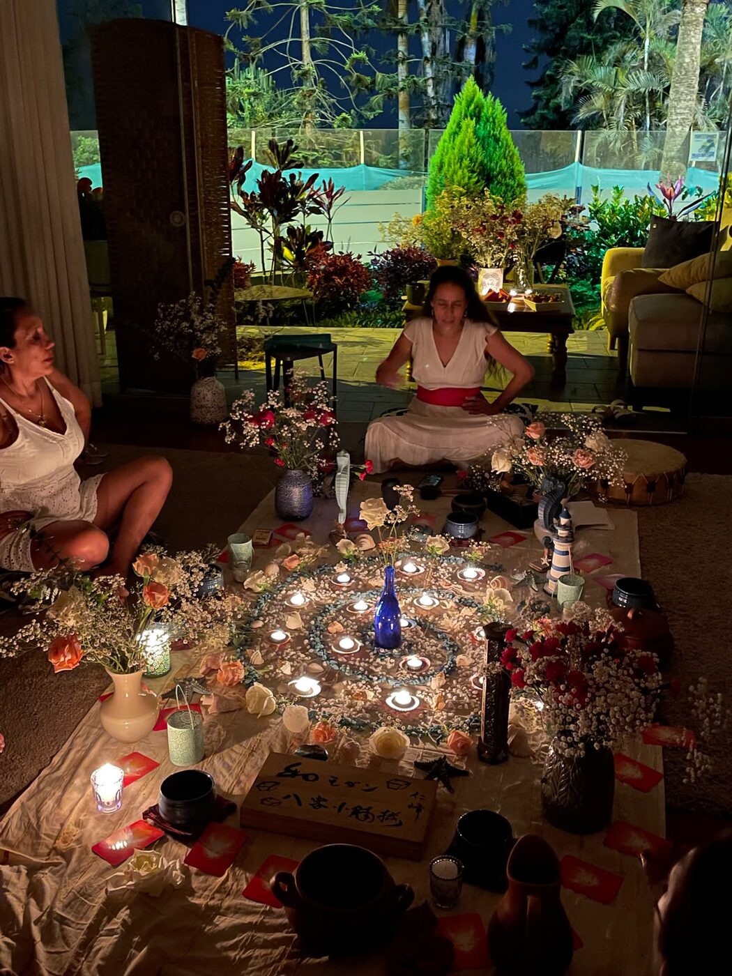 Ceremonia nocturna alrededor de un mandala de caracolas y velas, frente al jardín
